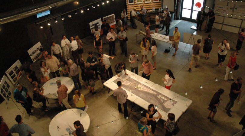 Community members engaged in a workshop at Arkins Park, discussing maps and plans on tables.