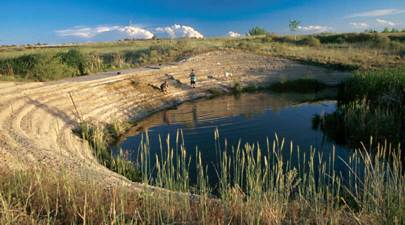 WATER_Shop-Creek: Two children playing near a small pond in a grassy landscape under a blue sky.