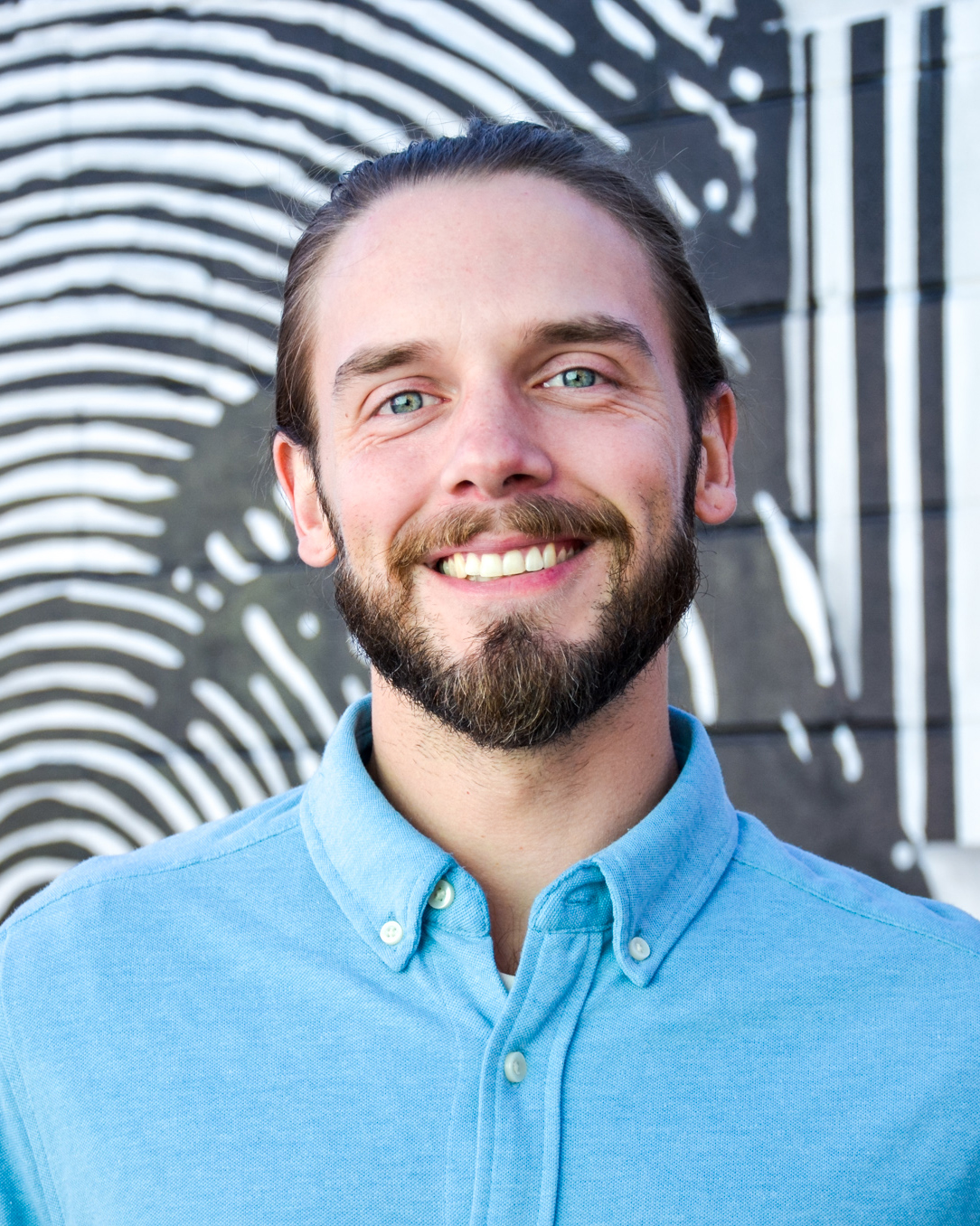 Will-Kern smiling, wearing a blue shirt, with a black-and-white abstract background